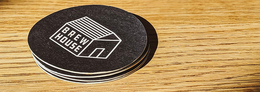 Mehrere Bierdeckel sind mit einem Logo bedruckt und liegen auf einem hölzernen Tisch